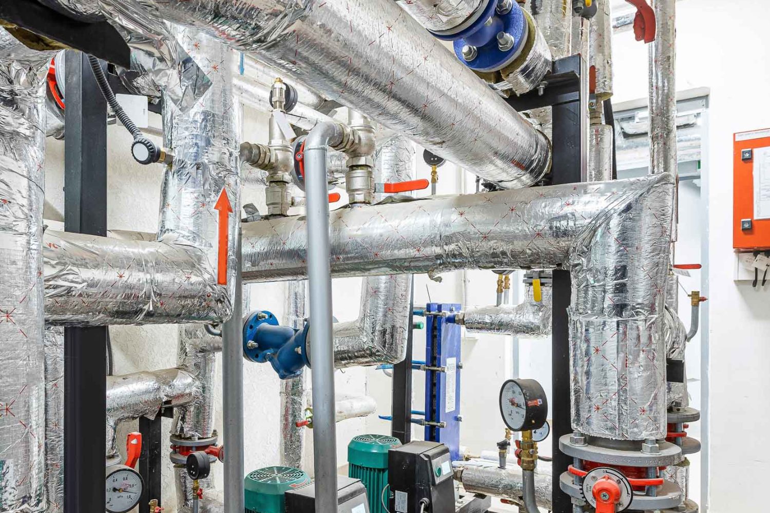 Industrial basement with heating pipes, pressure gauges, valves and heat exchangers.